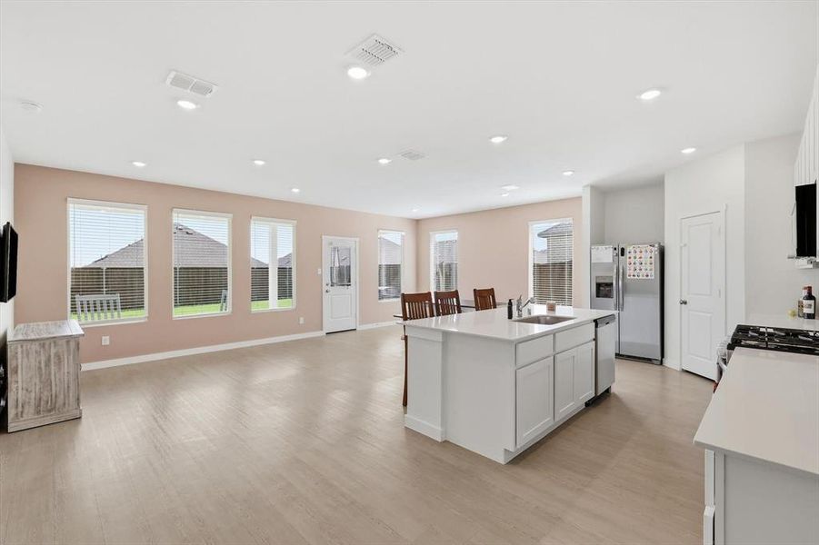 Open-concept living space featuring wood-finish flooring, recessed lighting, and a kitchen island with integrated sink Open-concept living space featuring wood-finish flooring, recessed lighting, and a kitchen island with integrated sink