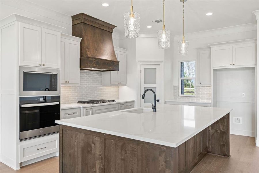 Kitchen featuring stainless steel appliances, a sink, a large island, custom exhaust hood, and backsplash