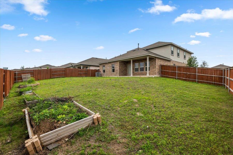 Spacious backyard featuring a brick and siding exterior, a covered patio, and a fully fenced perimeter