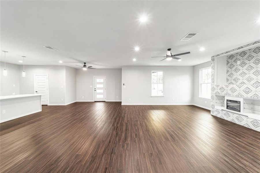 Unfurnished living room with a ceiling fan, dark wood-type flooring, a tile fireplace, recessed lighting, and healthy amount of natural light