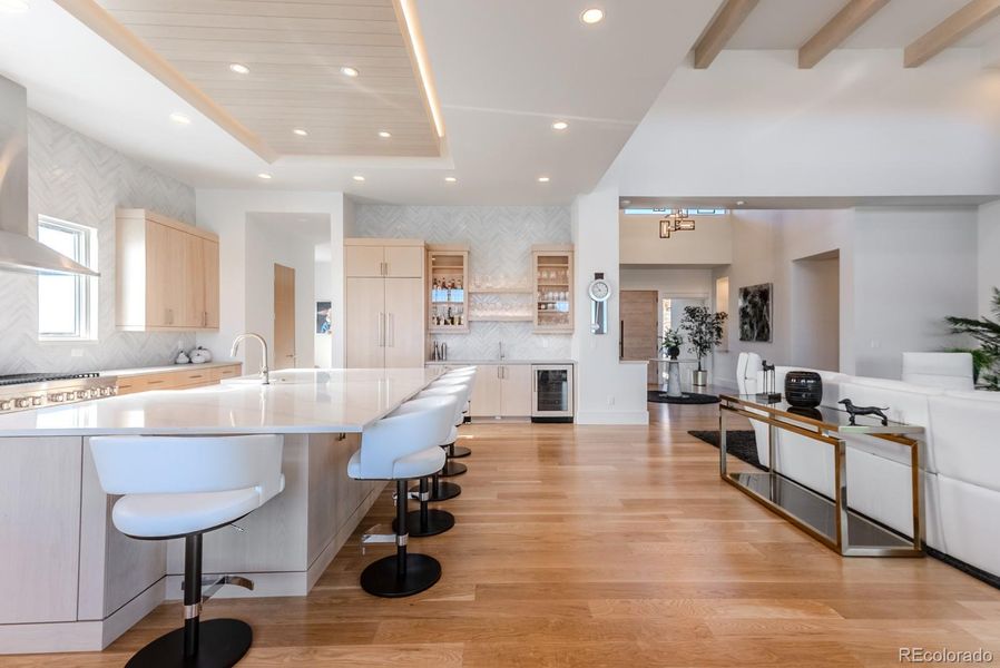 From the richness of the wide-plank oak floors to the commanding central island that anchors the room, and the wood-clad recessed ceiling washed in soft, integrated light above, the kitchen’s architecture is orchestrated with intention, depth, and visual impact at every level.