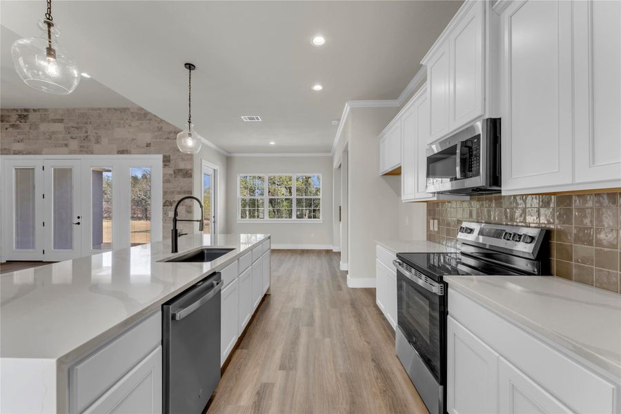 Kitchen featuring stainless steel appliances, white cabinets, light wood-style floors, a large island with sink, and ornamental molding