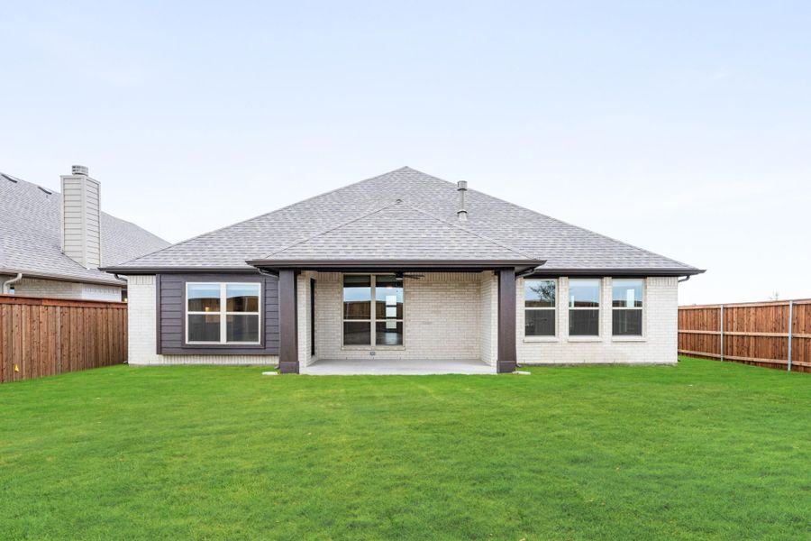 Rear exterior of single-story brick home with covered patio, large windows, and fenced backyard with green lawn Rear exterior of single-story brick home with covered patio, large windows, and fenced backyard with green lawn
