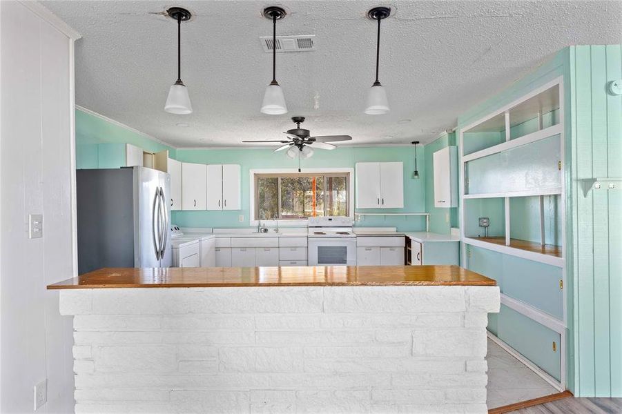 Kitchen with light countertops, white cabinets, freestanding refrigerator, white range oven, and a textured ceiling