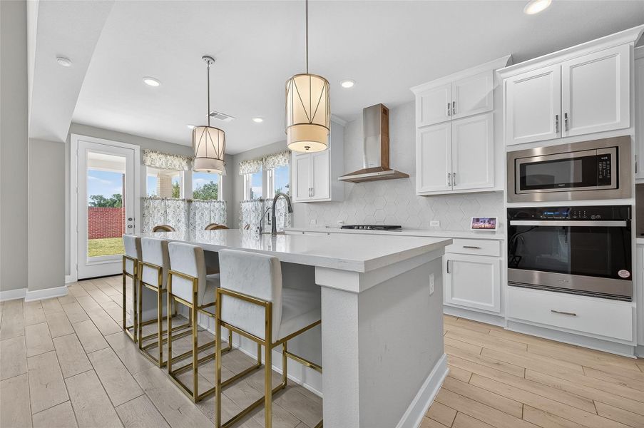 This stunning kitchen features white cabinetry, quartz countertops, and a gas cooktop with a sleek vent hood. The oversized island with brass-accented seating is perfect for casual dining or entertaining.