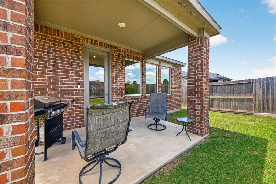Charming covered patio with brick accents, perfect for outdoor relaxation and entertaining, featuring comfortable seating and a convenient grill area overlooking a private fenced yard.