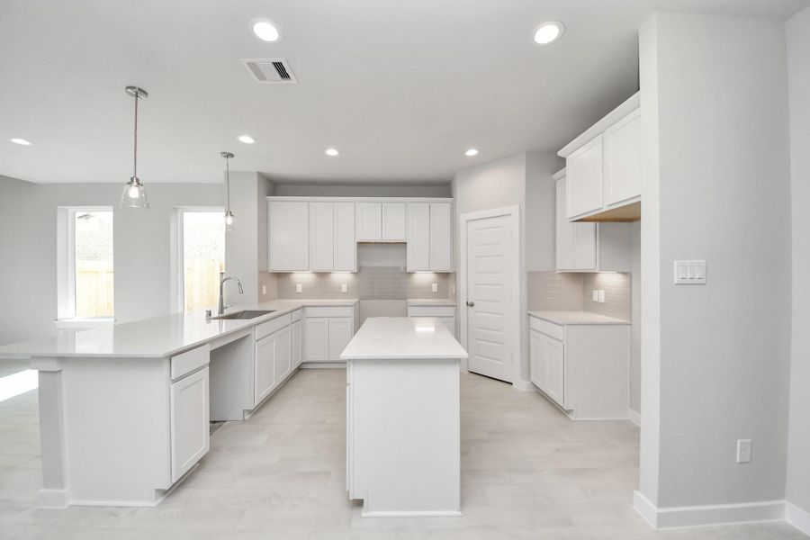 This kitchen is truly a chef's dream! This haven Boasts high ceilings, recessed & pendant lighting, stained wood cabinets, granite countertops, stainless steel appliances, a modern tile backsplash.  All of this overlooks your expansive family room, creating a perfect space for culinary delights and family gatherings. Sample photo of completed home with similar floor plan. Actual colors and selections may vary.