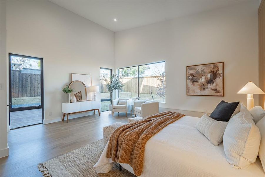 Bedroom featuring multiple windows, a towering ceiling, access to exterior, and light wood-type flooring