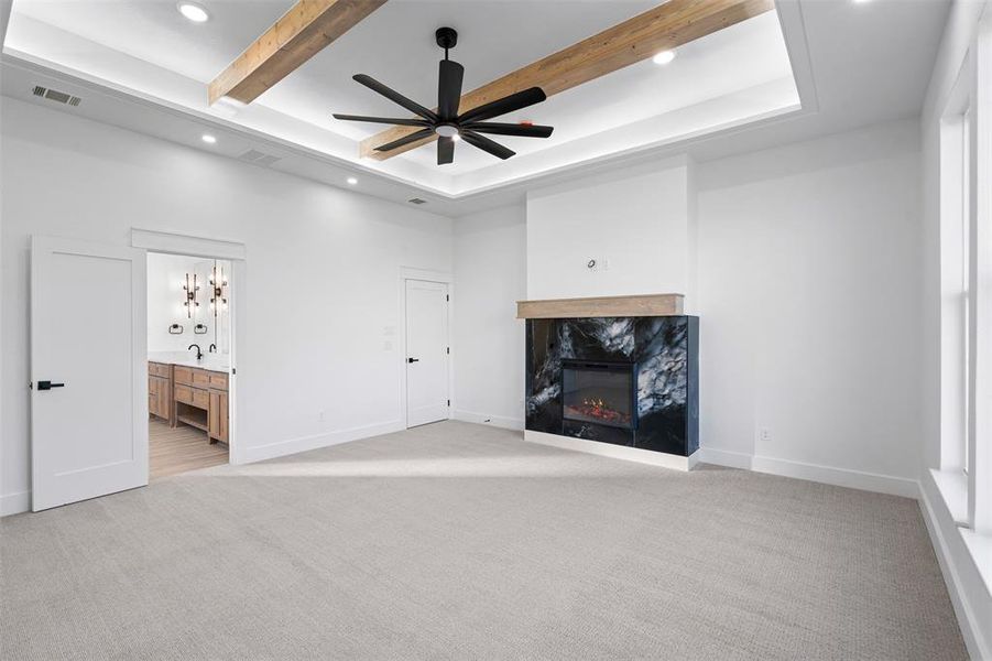 Unfurnished living room featuring sink, ceiling fan, a premium fireplace, beam ceiling, and light colored carpet