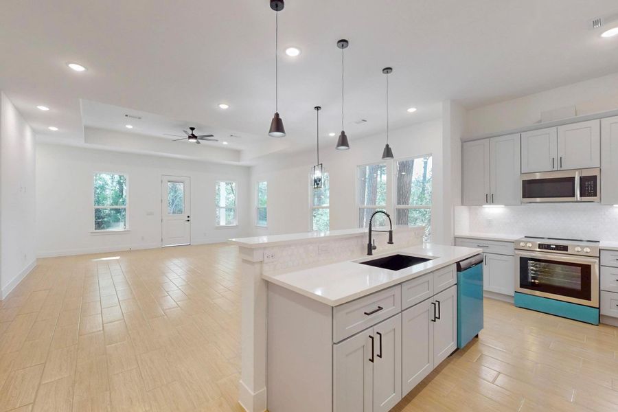 Kitchen featuring stainless steel appliances, decorative light fixtures, light wood-style floors, a kitchen island with sink, and open floor plan
