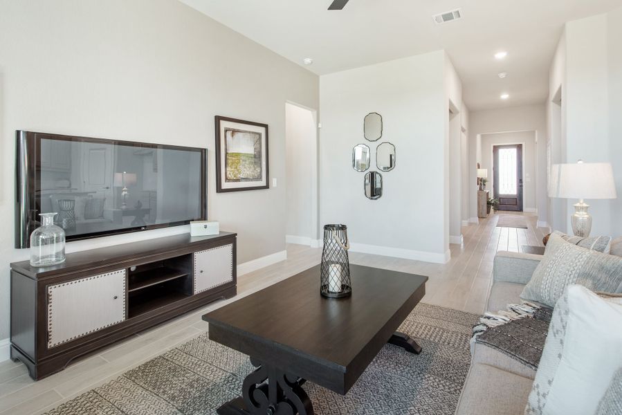Living room with wall-mounted TV, dark wood media console, coffee table, and hallway leading to front door. Living room with wall-mounted TV, dark wood media console, coffee table, and hallway leading to front door.