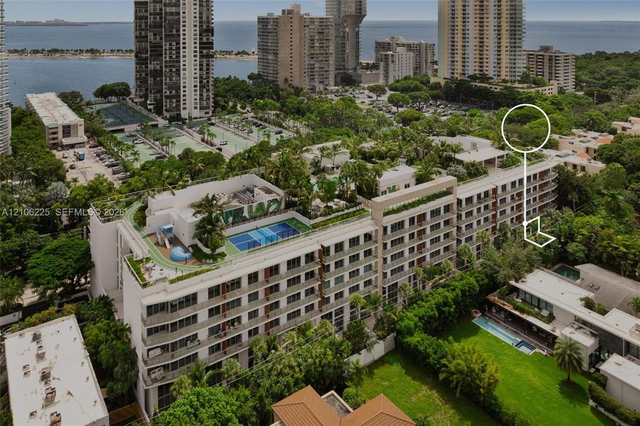 Aerial perspective of a multi-story residential building featuring a landscaped rooftop with a swimming pool, tennis court, and lush garden areas Aerial perspective of a multi-story residential building featuring a landscaped rooftop with a swimming pool, tennis court, and lush garden areas