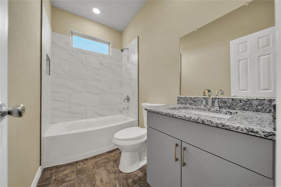 Full bathroom with tile patterned floors, vanity, tiled shower / bath, and toilet