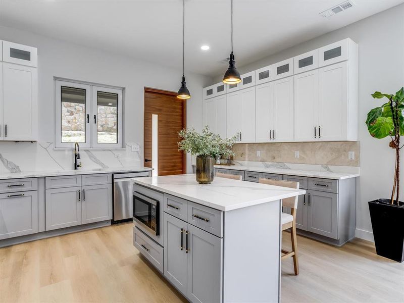 Modern kitchen featuring a central island with integrated microwave, white countertops, and light wood-finish flooring Modern kitchen featuring a central island with integrated microwave, white countertops, and light wood-finish flooring