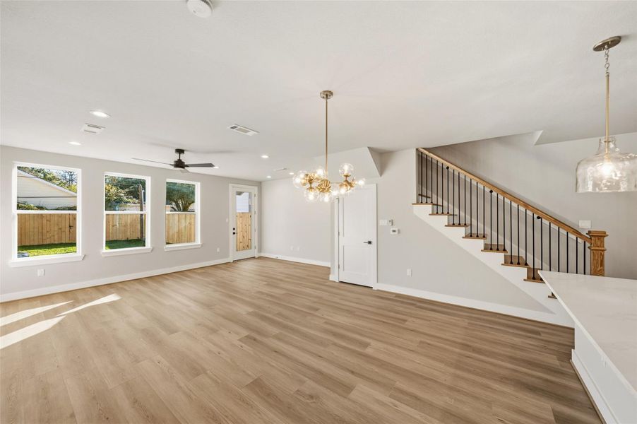 Bright and spacious open-plan living area with large windows, modern light fixtures, and a ceiling fan. Features a stylish staircase. Ideal for family gatherings.