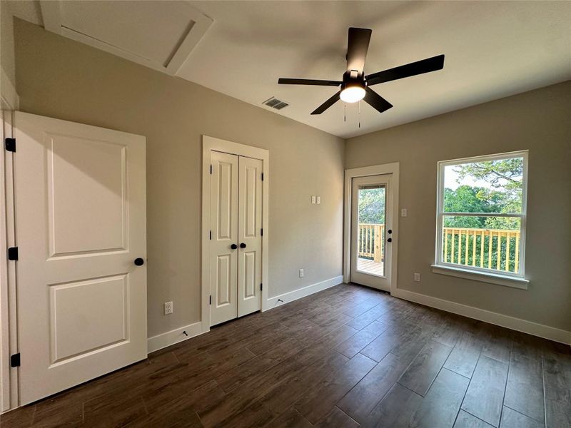 Unfurnished bedroom featuring access to exterior, dark wood-style floors, attic access, a ceiling fan, and a closet