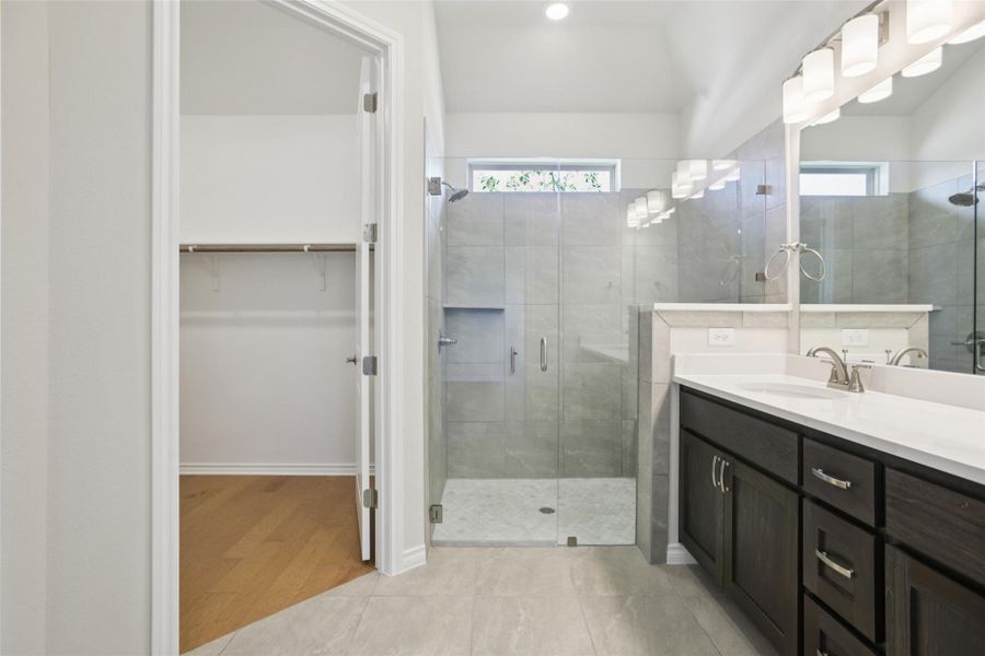 Full bath featuring vanity, a spacious closet, a shower stall, and light tile patterned floors Full bath featuring vanity, a spacious closet, a shower stall, and light tile patterned floors