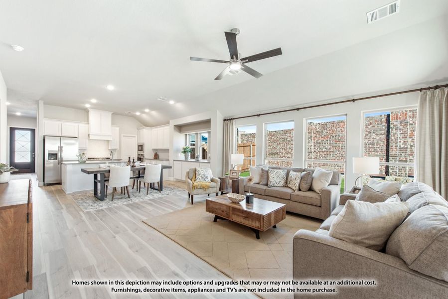 Open-concept living room with ceiling fan, light wood floors, and kitchen visible in background Open-concept living room with ceiling fan, light wood floors, and kitchen visible in background