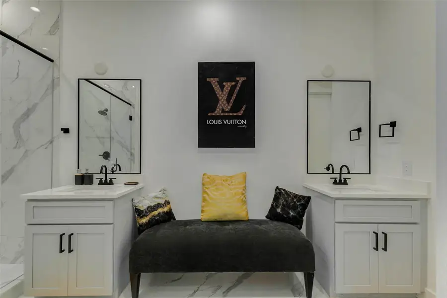 Stylish primary bath with dual vanities, black-framed mirrors, matte black fixtures, white cabinetry, marble-look tile, and a glass shower. The balanced layout and crisp white-and-black design create a polished, boutique-inspired space with a bright, contemporary look.