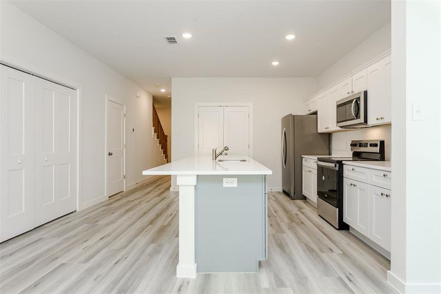 Kitchen with light hardwood / wood-style floors, sink, a kitchen island with sink, white cabinetry, and appliances with stainless steel finishes