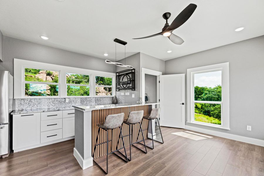 Kitchen area featuring wood-finish flooring, white cabinetry, a patterned tile backsplash, and an integrated breakfast bar with a slatted wood-panel front