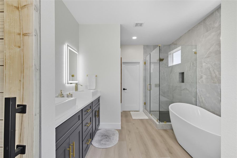 Full bath with a freestanding bath, double vanity, a marble finish shower, and light wood-type flooring