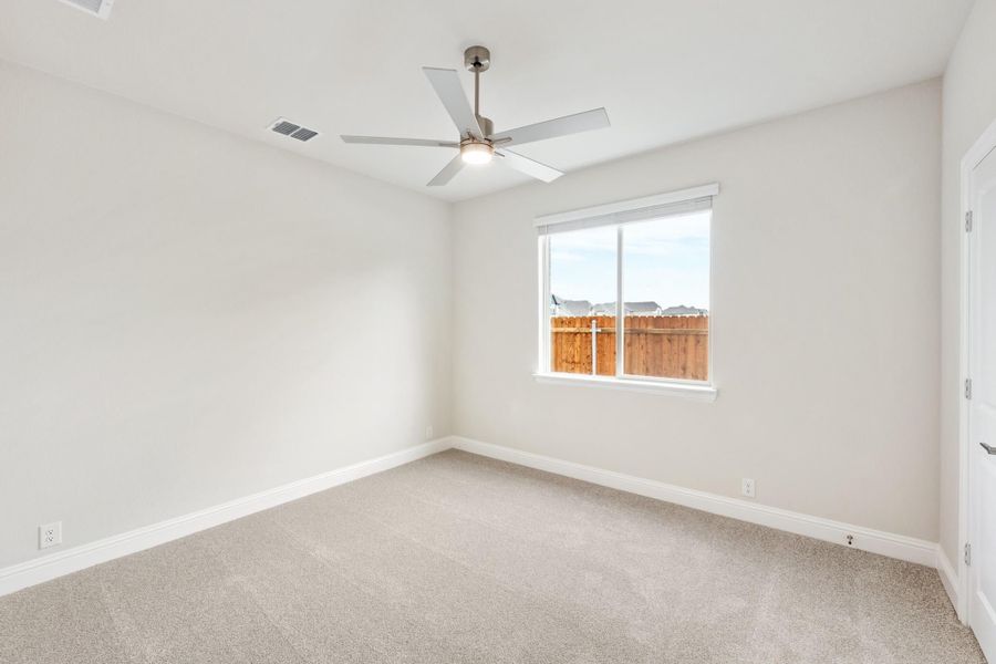 Empty bedroom with beige carpet, ceiling fan, and single window with backyard view