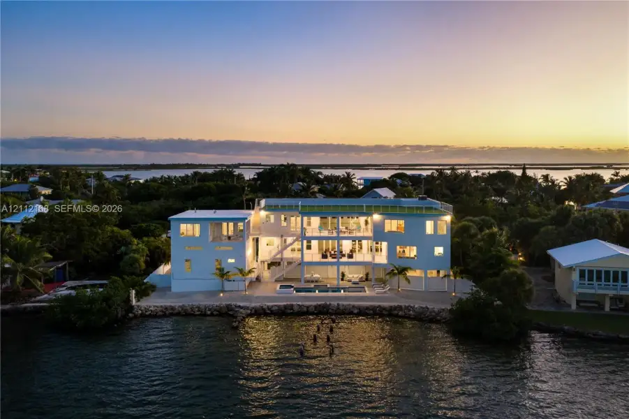 Waterfront residence featuring multi-level balconies, an in-ground swimming pool, a rock-lined shoreline, and a rooftop terrace Waterfront residence featuring multi-level balconies, an in-ground swimming pool, a rock-lined shoreline, and a rooftop terrace