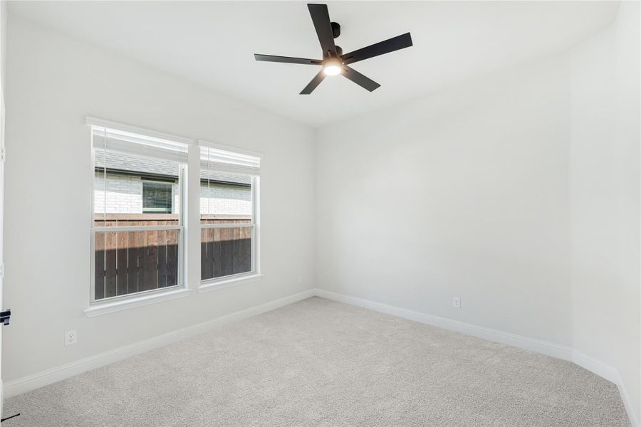 Empty bedroom with carpet flooring, black ceiling fan, and double windows with white trim