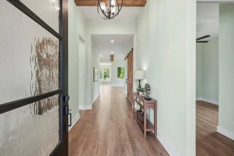 Upon entering the home, guests are greeted by soaring ceilings accented with rustic wood beams, rich upgraded LVP flooring, and a sophisticated neutral color palette that creates an inviting sense of warmth and openness. The expansive main living area naturally draws the eye forward, where large windows beautifully frame the lush Backyard, seamlessly blending indoor comfort with serene outdoor views.