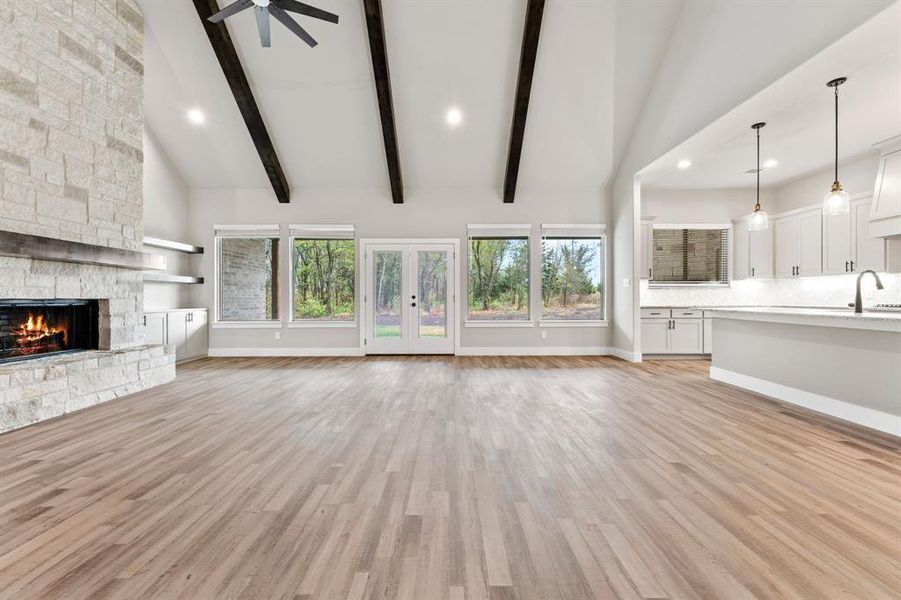 Unfurnished living room with light hardwood / wood-style floors, sink, high vaulted ceiling, beam ceiling, and a fireplace