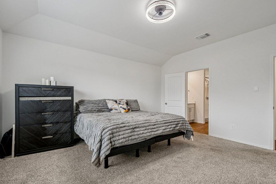 Bedroom featuring light colored carpet, vaulted ceiling, and connected bathroom