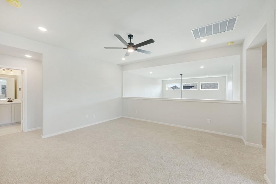 Spacious empty bedroom with carpet, ceiling fan, recessed lighting, and an attached bathroom visible through doorway.