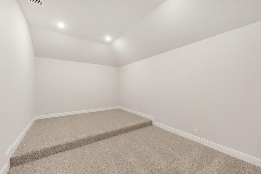 Empty room with beige carpet, white walls, recessed lighting, and a raised carpeted platform area.