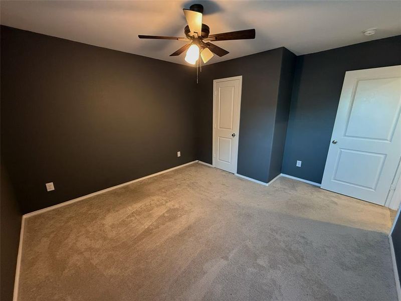 Carpeted room featuring dark walls, white trim, and a ceiling fan with integrated lighting Carpeted room featuring dark walls, white trim, and a ceiling fan with integrated lighting