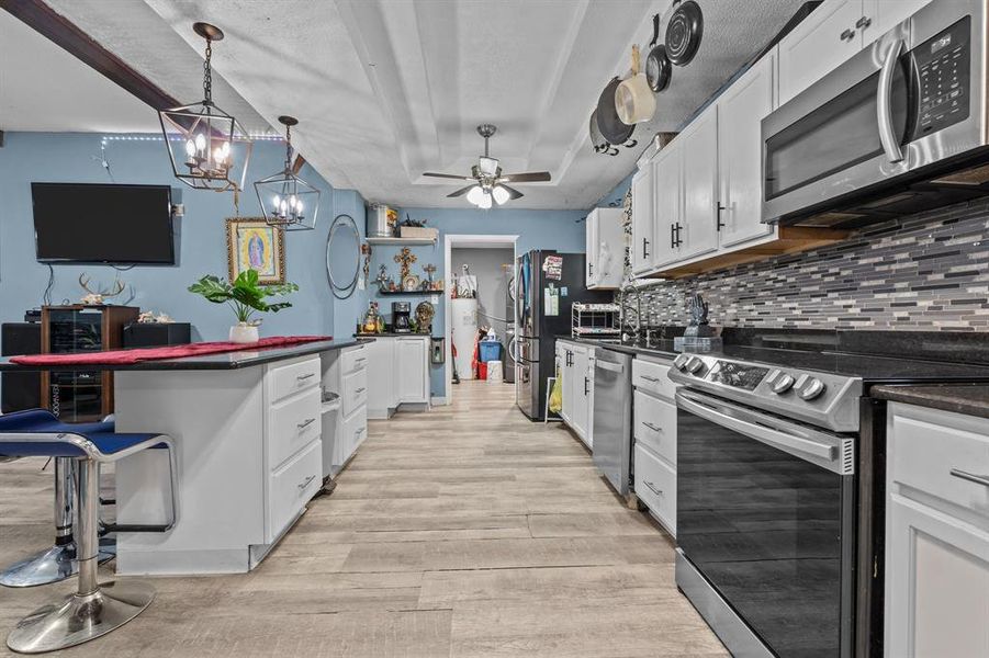 Kitchen with hanging light fixtures, white cabinets, stainless steel appliances, and light wood-type flooring