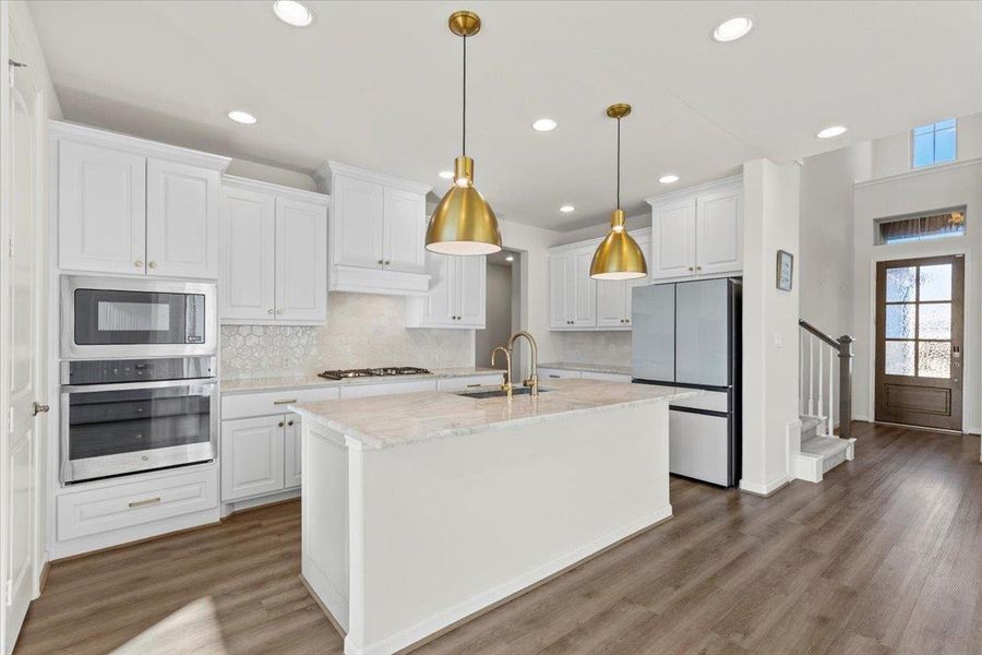 Kitchen with appliances with stainless steel finishes, white cabinetry, backsplash, a kitchen island with sink, and decorative light fixtures Kitchen with appliances with stainless steel finishes, white cabinetry, backsplash, a kitchen island with sink, and decorative light fixtures