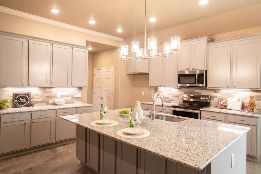 Kitchen featuring a notable chandelier, appliances with stainless steel finishes, a sink, decorative backsplash, and ornamental molding