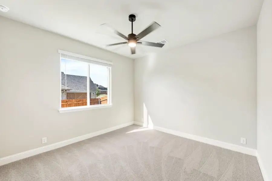 Empty bedroom with carpet flooring, ceiling fan with light, and single window with backyard view