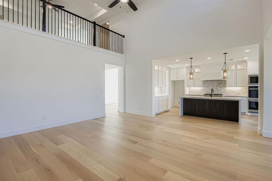 Unfurnished living room with ceiling fan, light wood-style floors, a high ceiling, and recessed lighting