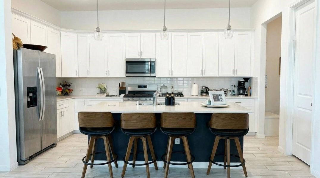 Bright, modern kitchen with sleek white cabinets and stainless steel appliances. Features a spacious island with seating for four and pendant lighting, providing a stylish and functional space for cooking and entertaining. Bright, modern kitchen with sleek white cabinets and stainless steel appliances. Features a spacious island with seating for four and pendant lighting, providing a stylish and functional space for cooking and entertaining.