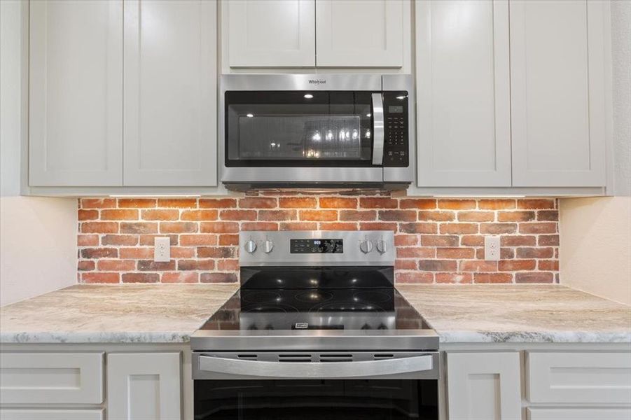 Kitchen featuring stainless steel appliances, tasteful backsplash, and light stone counters