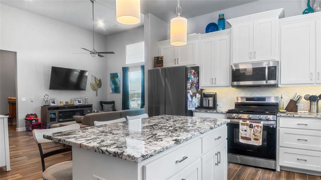 Kitchen with decorative light fixtures, dark hardwood / wood-style floors, stainless steel appliances, backsplash, and a center island