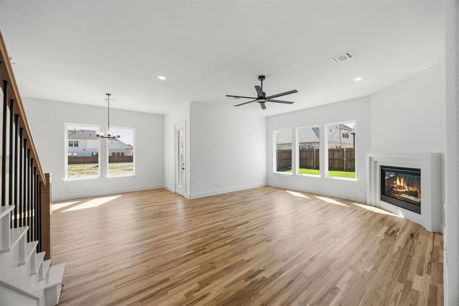 Unfurnished living room with a glass covered fireplace, a chandelier, light wood-type flooring, and ceiling fan