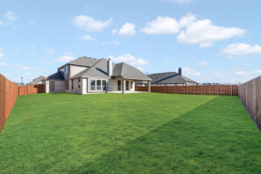 Large backyard with green lawn, wood privacy fence, and brick home with covered patio in background