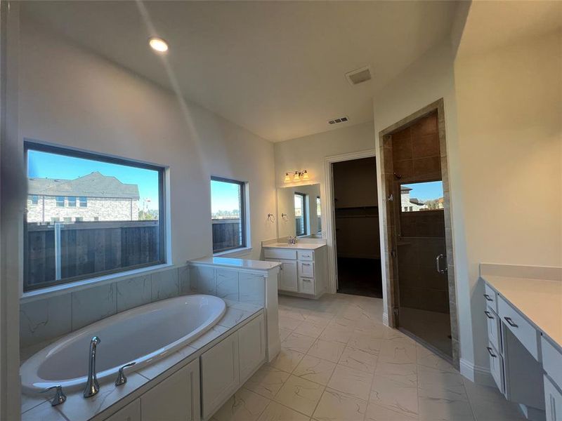 Full bath with a stall shower, visible vents, marble finish floor, His & hers vanity, and a garden tub.