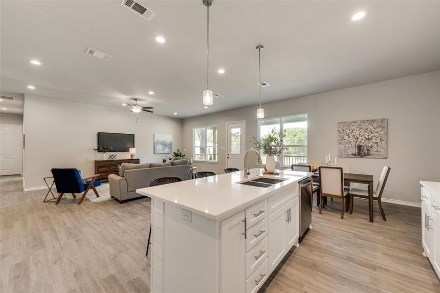 Kitchen with a center island with sink, sink, stainless steel dishwasher, ceiling fan, and decorative light fixtures