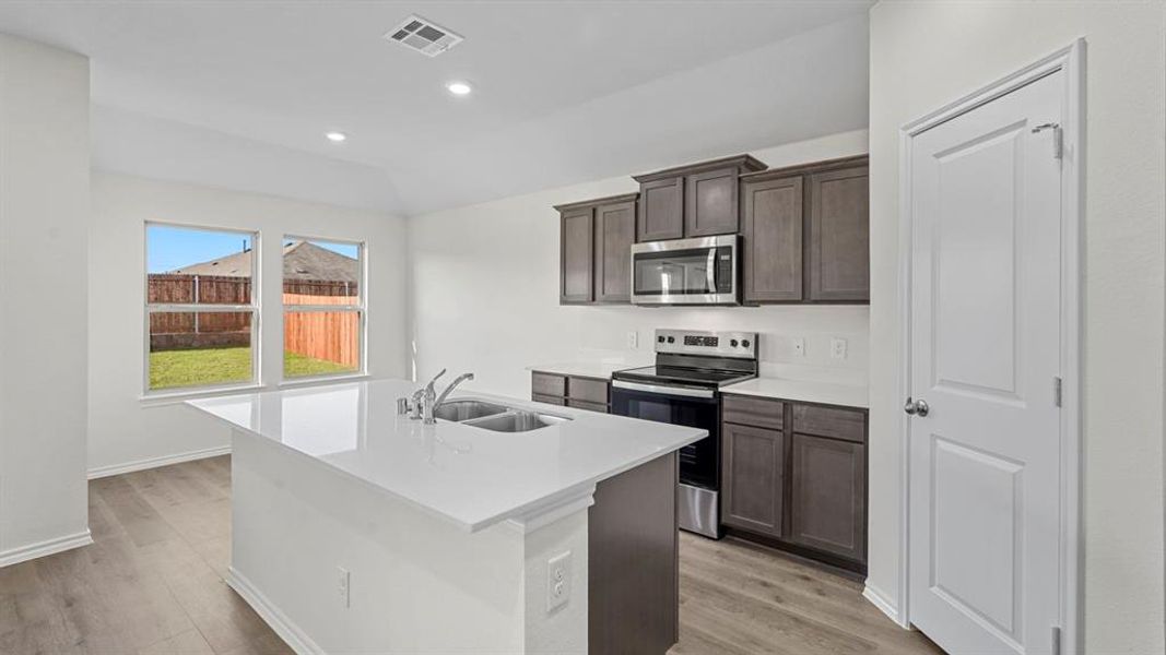 Kitchen featuring stainless steel appliances, a kitchen island with sink, light wood-style floors, dark wood finish cabinets, and recessed lighting