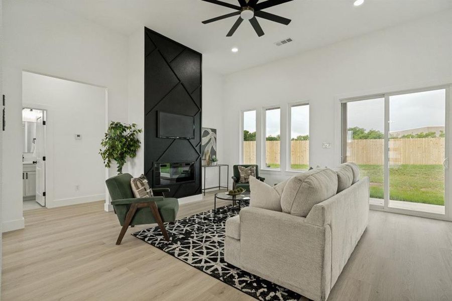 Expansive living area featuring light wood-finish flooring, a contemporary black accent wall with an integrated fireplace, and a ceiling fan Expansive living area featuring light wood-finish flooring, a contemporary black accent wall with an integrated fireplace, and a ceiling fan