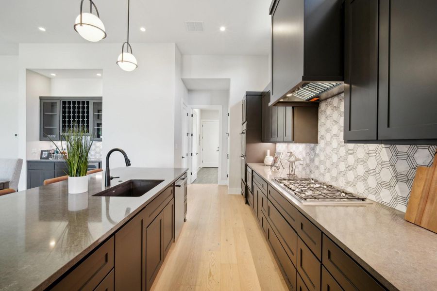 Kitchen with wall chimney exhaust hood, sink, decorative light fixtures, tasteful backsplash, and light stone counters.